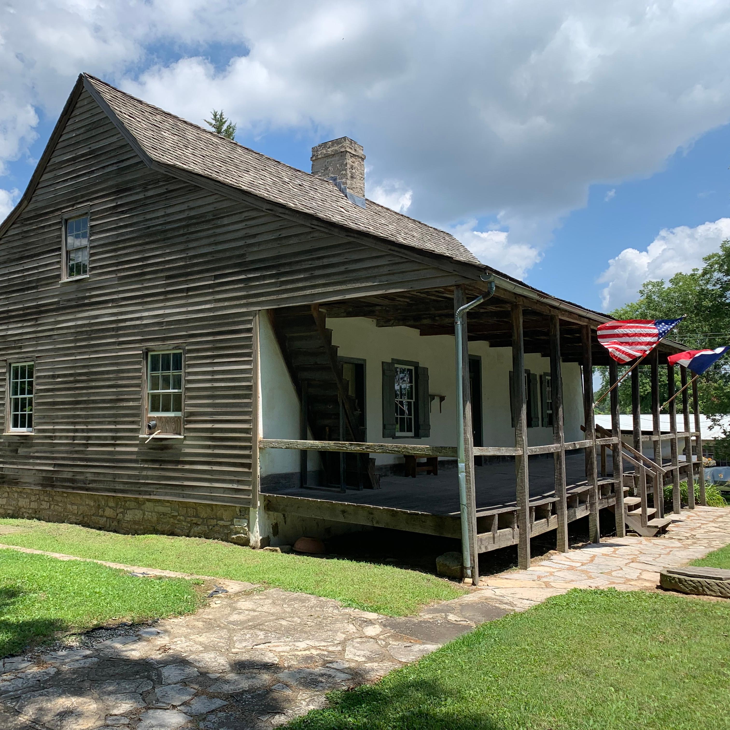 Wood frame house with triangular roof and U.S. and French flags flying in front. 