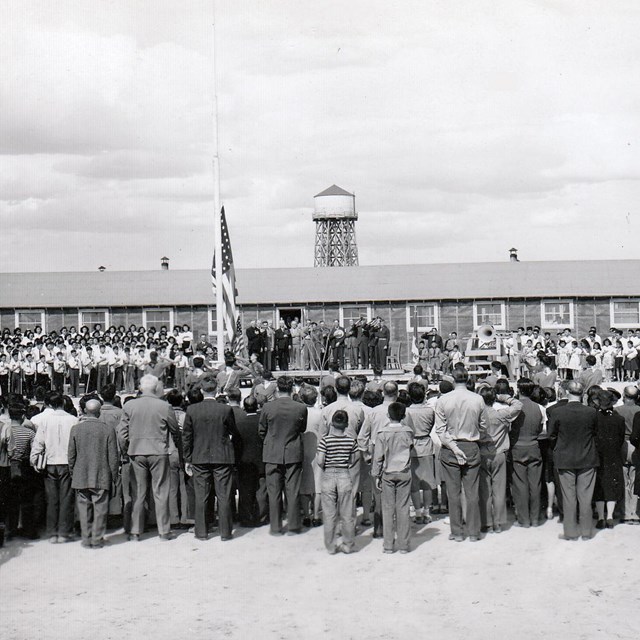 Black and white image of incarcerees standing in front of a barrack.