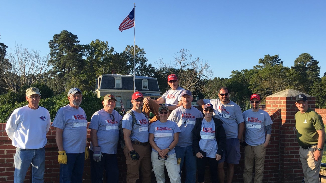 Eleven veteran volunteers gather along a brick wall.