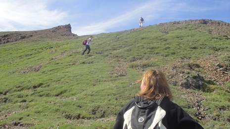 a woman wearing a day pack watches to others hiking up a mountain