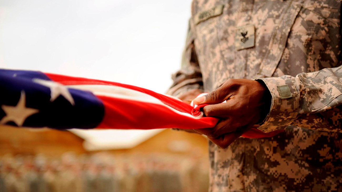 Two people in army fatigues fold American flag.