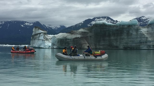 A raft full of people in Alsek Lake with Glaciers in the background.