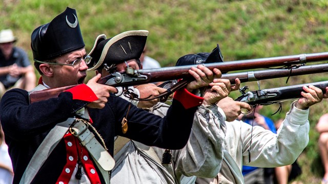 men in colonial uniforms firing muskets