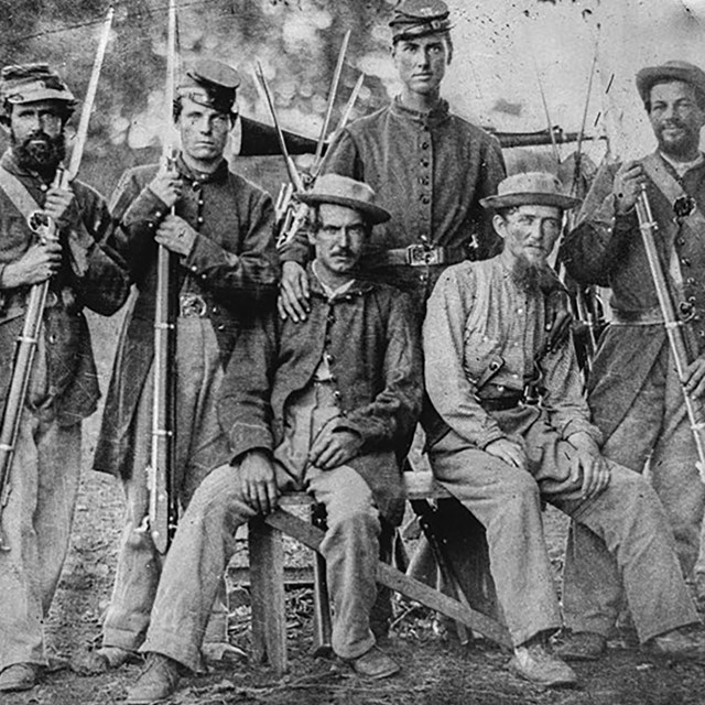 Civil War soldiers pose for camera in uniforms and holding weapons.