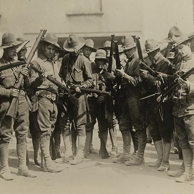 World War I soldiers in uniform, examining new rifles. 