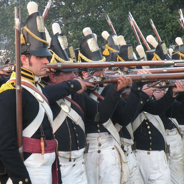 men in dark blue uniforms firing muskets