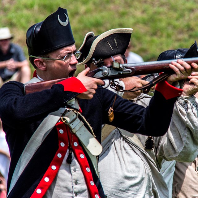 men in colonial uniforms firing muskets