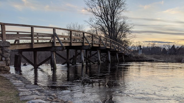 A wooden bridge spans a small river at sunset