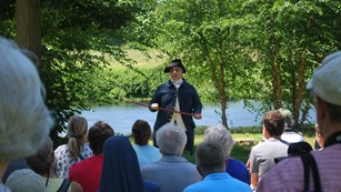 A park ranger in colonial clothing speaks to a large group of visitors