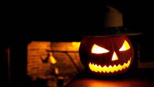 A Jack-'o'-Lantern with Ranger flat hat on sits on a table before a colonial fireplace 
