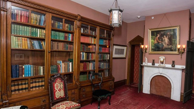 Library of The Wayside. 19th Century study with a red carpet, book shelves and a marble fireplace