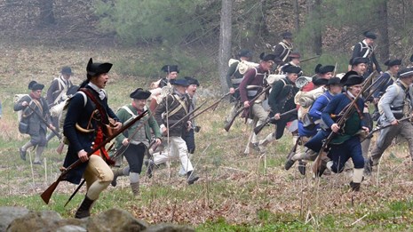 A group of minute men charge across an open field. 