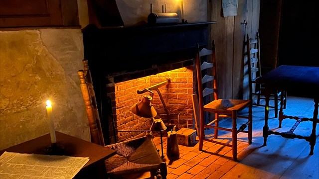 A night scene inside a historic house with fireplace illuminating the room
