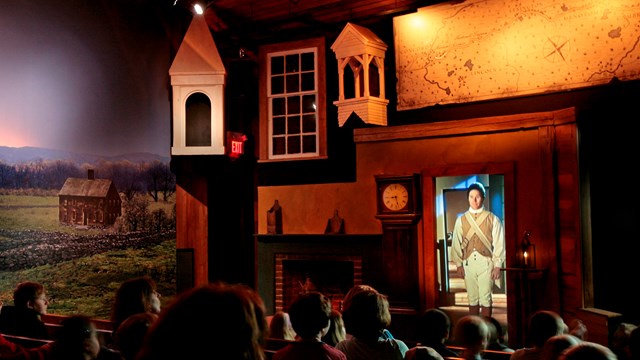 Visitors sitting in a darkened theater with lighted multimedia elements