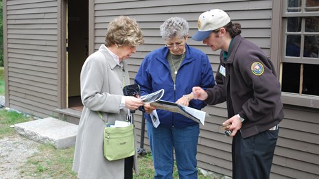 A park volunteer in brown sweater with volunteer patch gives directions to visitors.