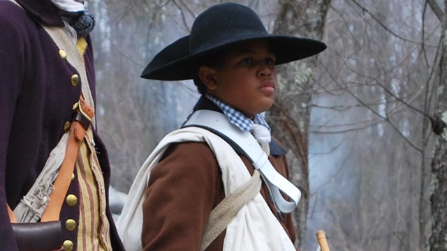 Young Black man with a military drum standing next to a young white man with a fife.