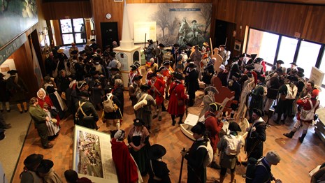 A group of Living History Volunteers in costume stand in a visitor center lobby.