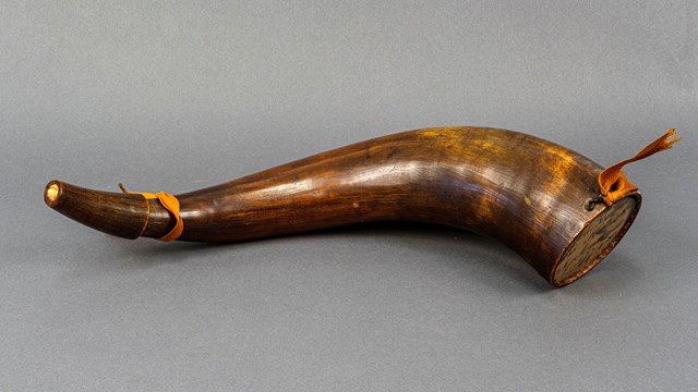 A brown and tan powder horn with orange ribbon tied to the ends.