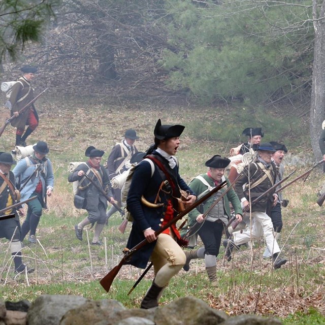 A group of minute men charge across an open field. 