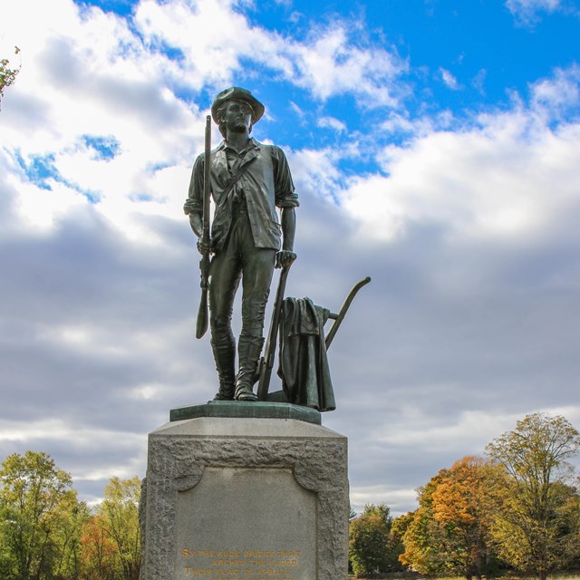 A bronze statue of a minute man holding a musket rest on a stone base with inscription.