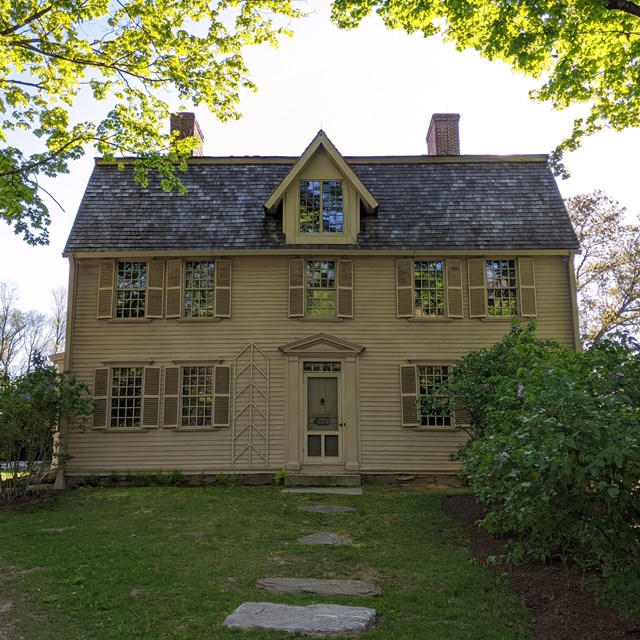 A colonial house with two stories and a central door. There are bushes at the edge of the home.