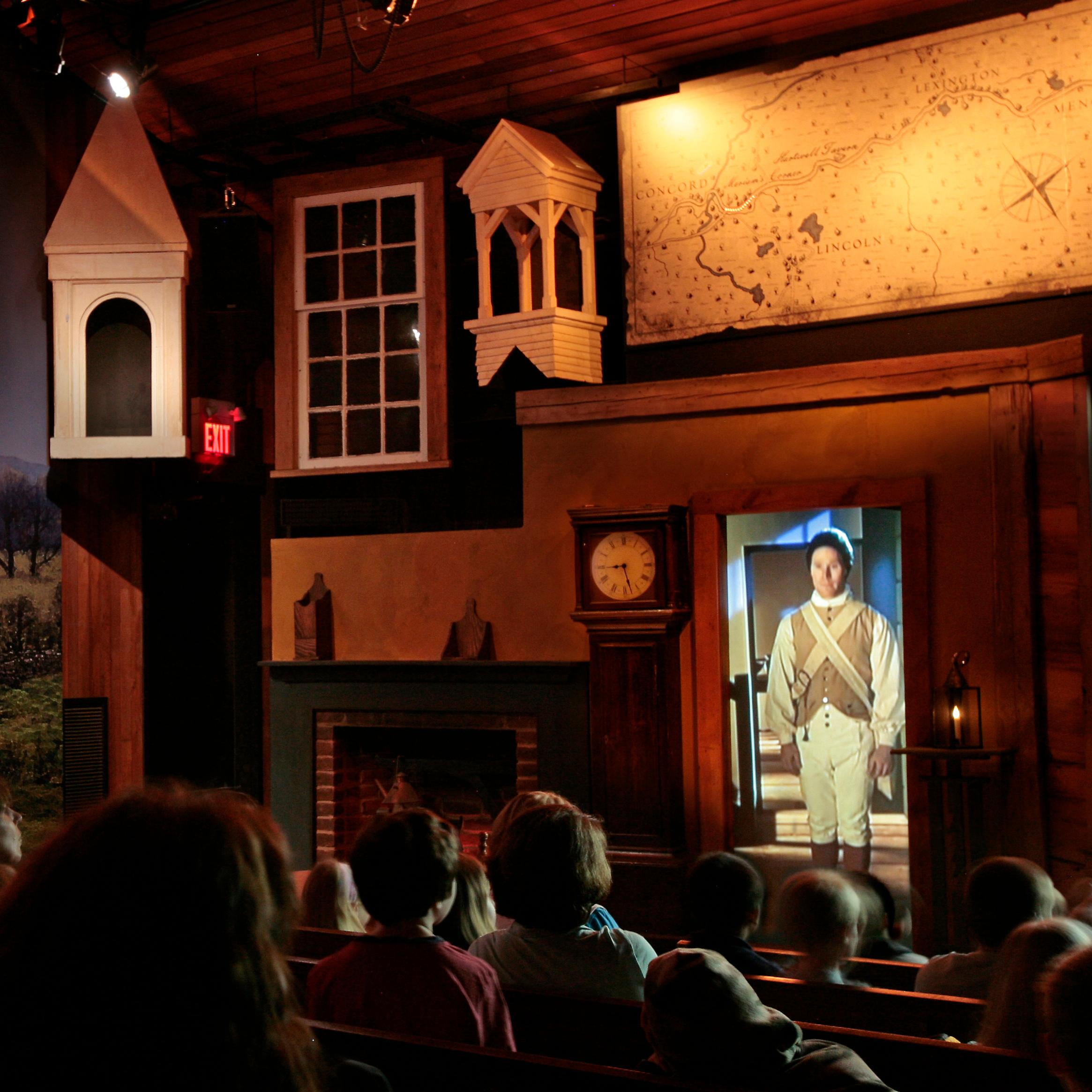 Visitors sitting in a darkened theater with lighted multimedia elements