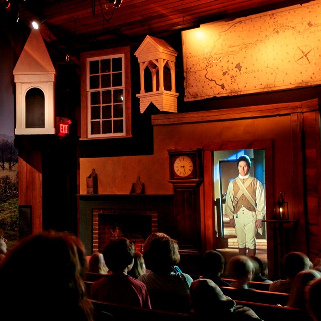 Visitors sitting in a darkened theater with lighted multimedia elements