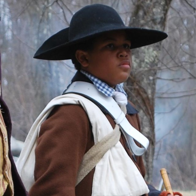 Young black man with a military drum standing next to a young white man with a fife.