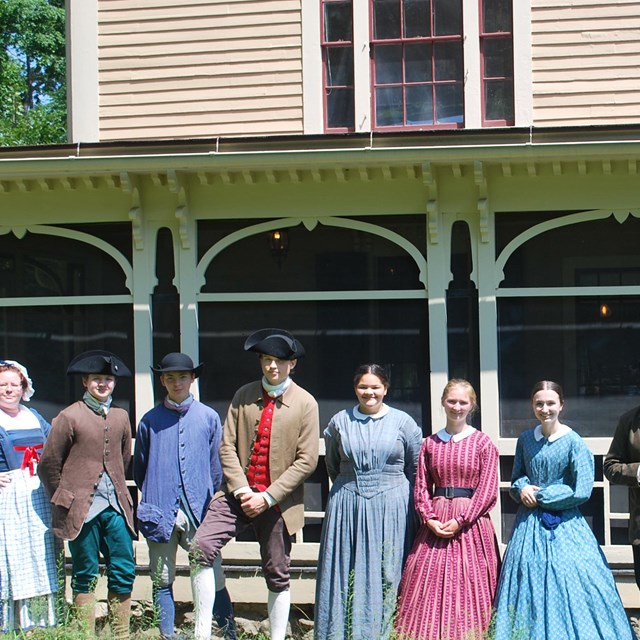 people dressed in 18th and 19th century clothing stand outside a screened porch