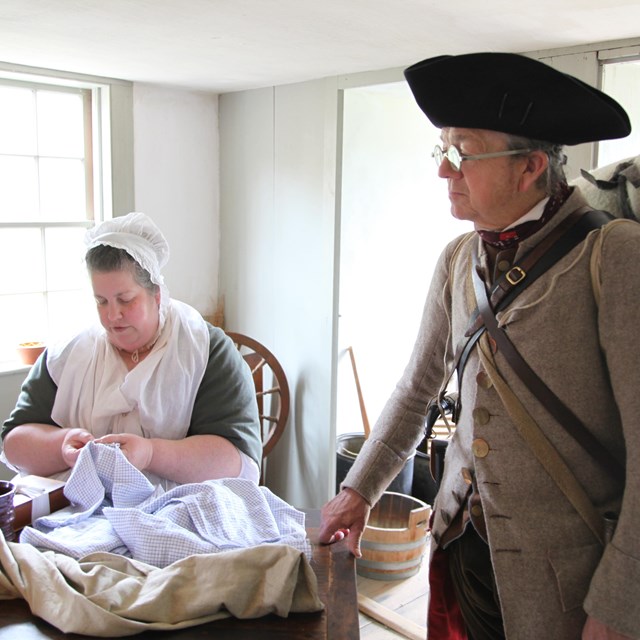 Park volunteers dressed in Colonial clothing work on a sewing project and present to a group