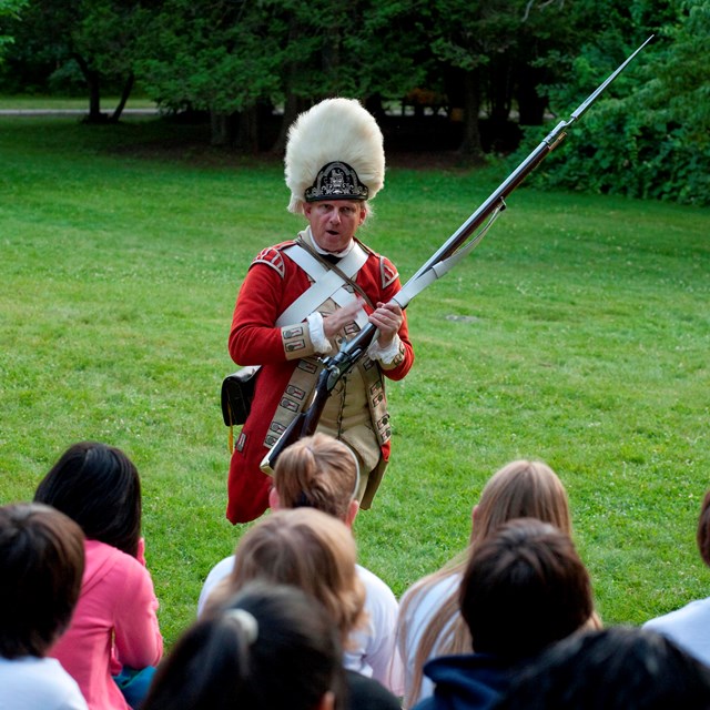 A British Soldiers stands in front of students and explains a musket