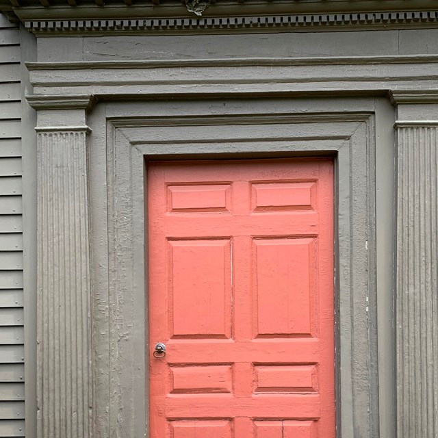 Red wooden door framed with wide wooden pediments painted brown