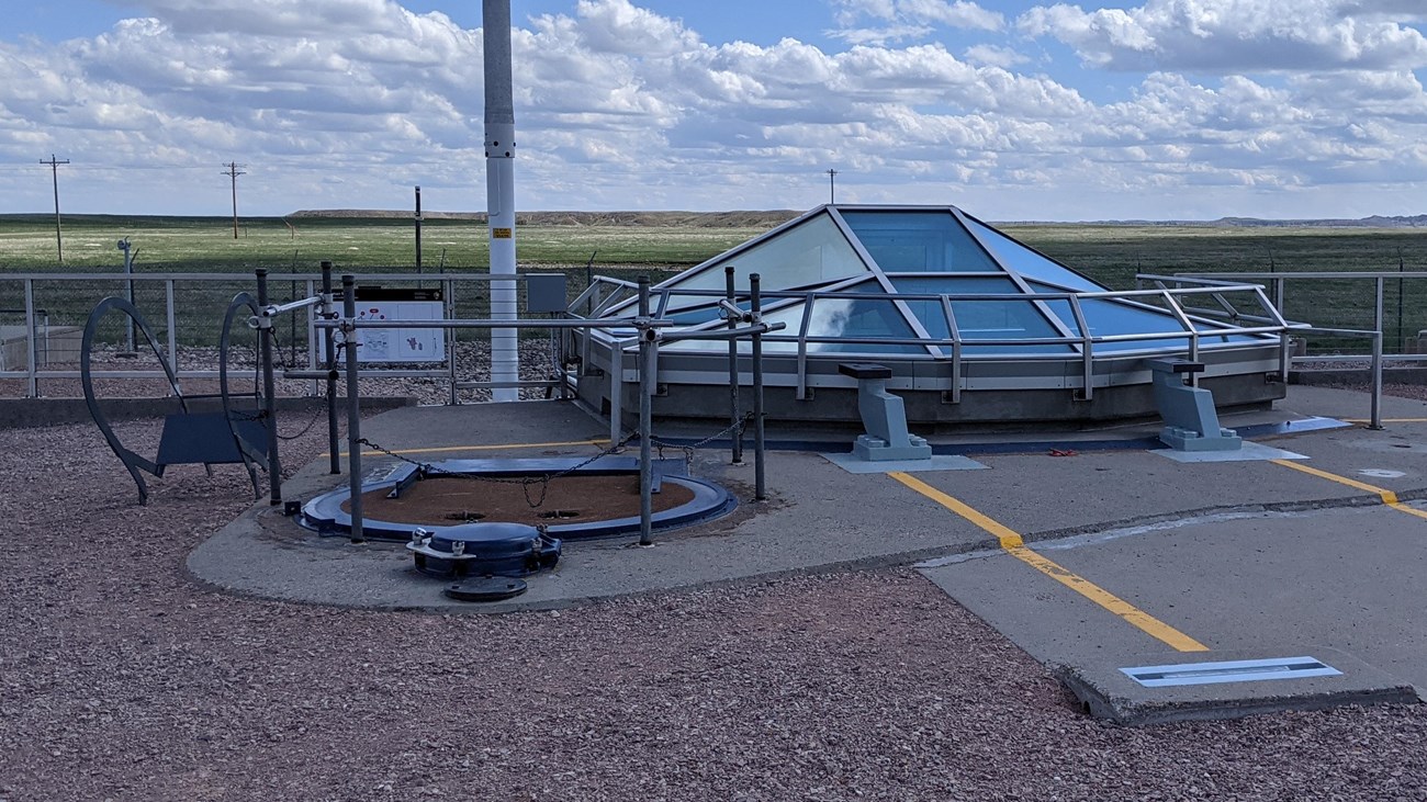 Glass dome inside a chainlink compound covered by gravel in the middle of a prairie