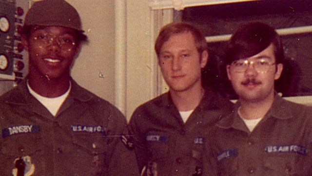 Men in green uniforms stand in a room