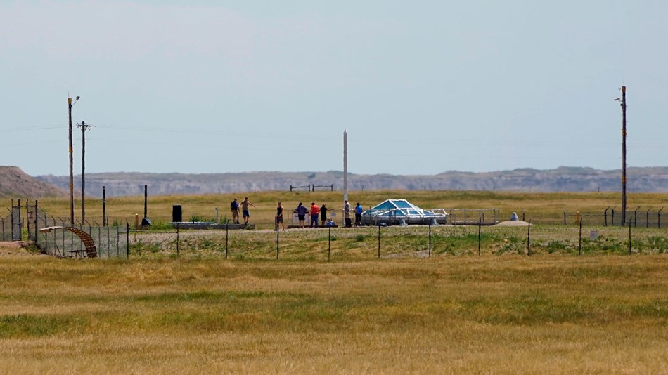 People stand inside a fenced compound on a prairie landscape