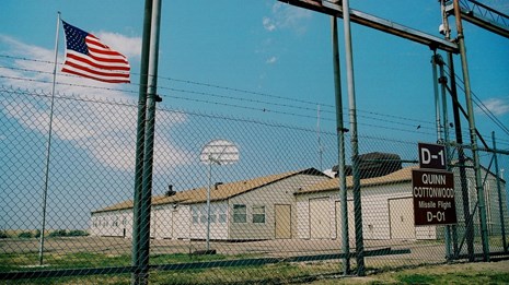 An American flag flys in front of a building inside a high fence
