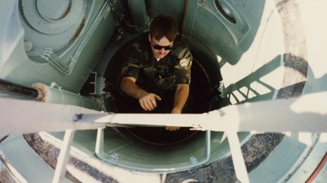 Airman climbing a ladder out of a cylindrical hatchway. 