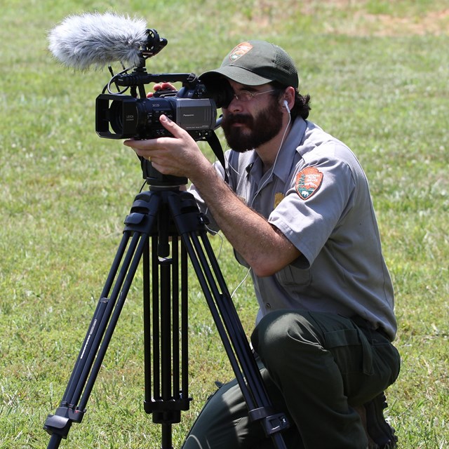 Ranger kneels behind video camera on tripod