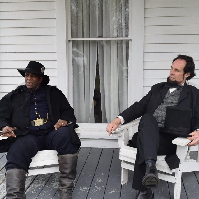 Civil War living history actors sit together on porch of historic building