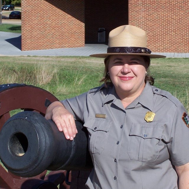 Smiling ranger leans on cannon outside brick building