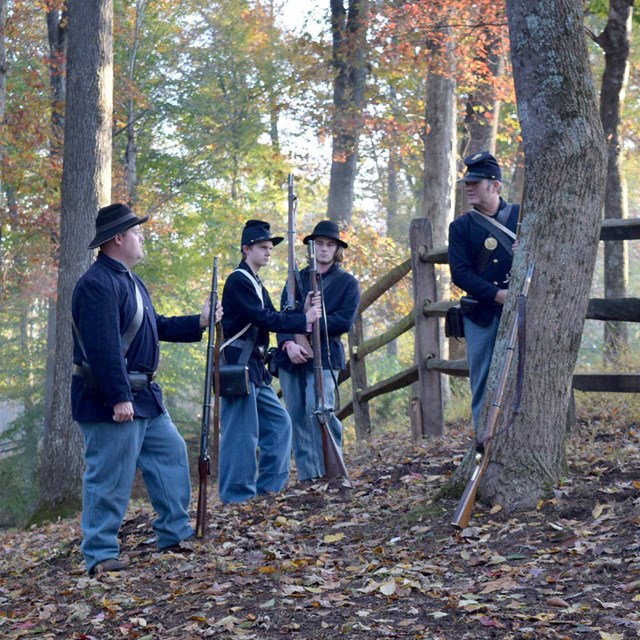 Group of union reenactors chat by fence in forest