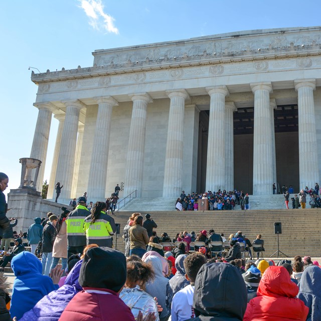 Crowd watching a school group behind a podium on the steps of the Lincoln Memorial