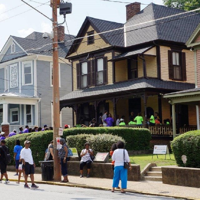 Visitors gathered outside of a two-story yellow house on a neighborhood street