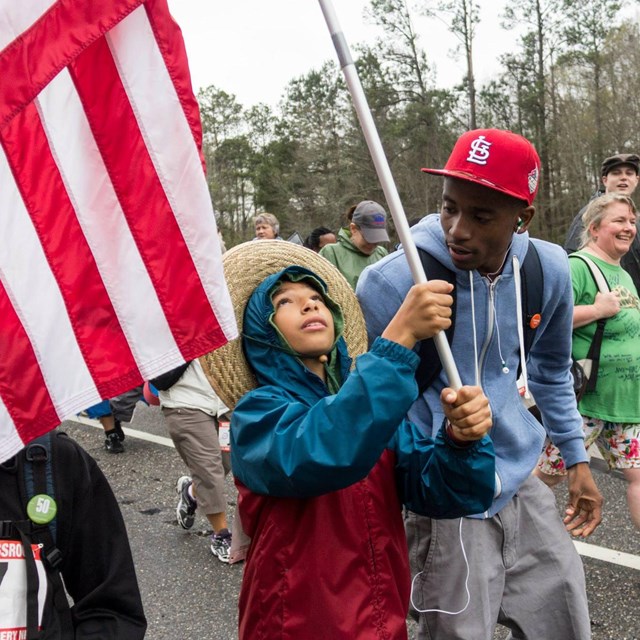 Man talking to a child holding a US flag as they march in the street 