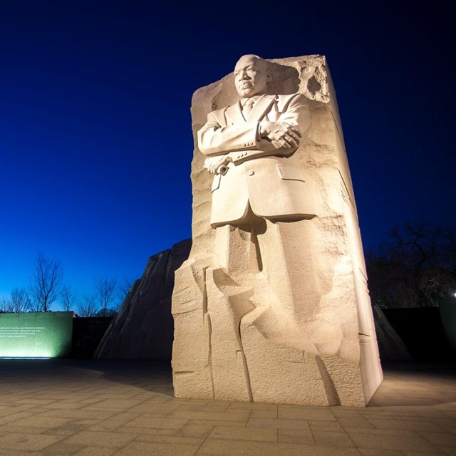 Statue of Martin Luther King Jr. and a memorial wall lit up at night