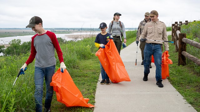 Five people carrying trash bags and grabbers walk down a concrete path