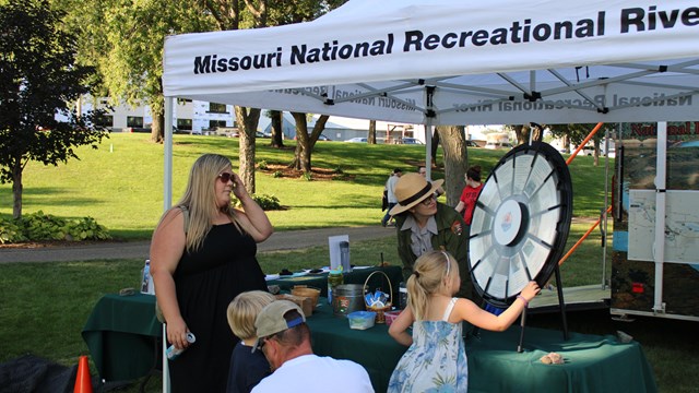 A park ranger talks with a family at an outdoor event. 