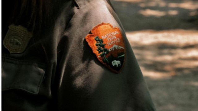NPS Arrowhead on grey shirt near park ranger gold badge. 