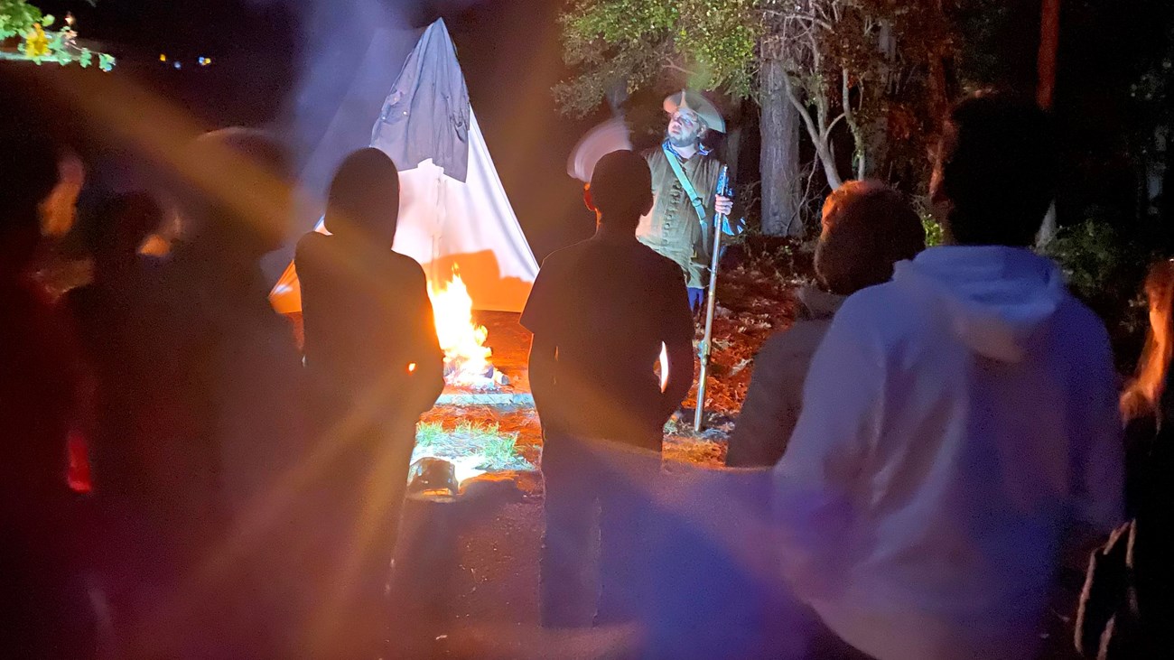 Man dressed in colonial clothing standing outside a tent surrounded by people.