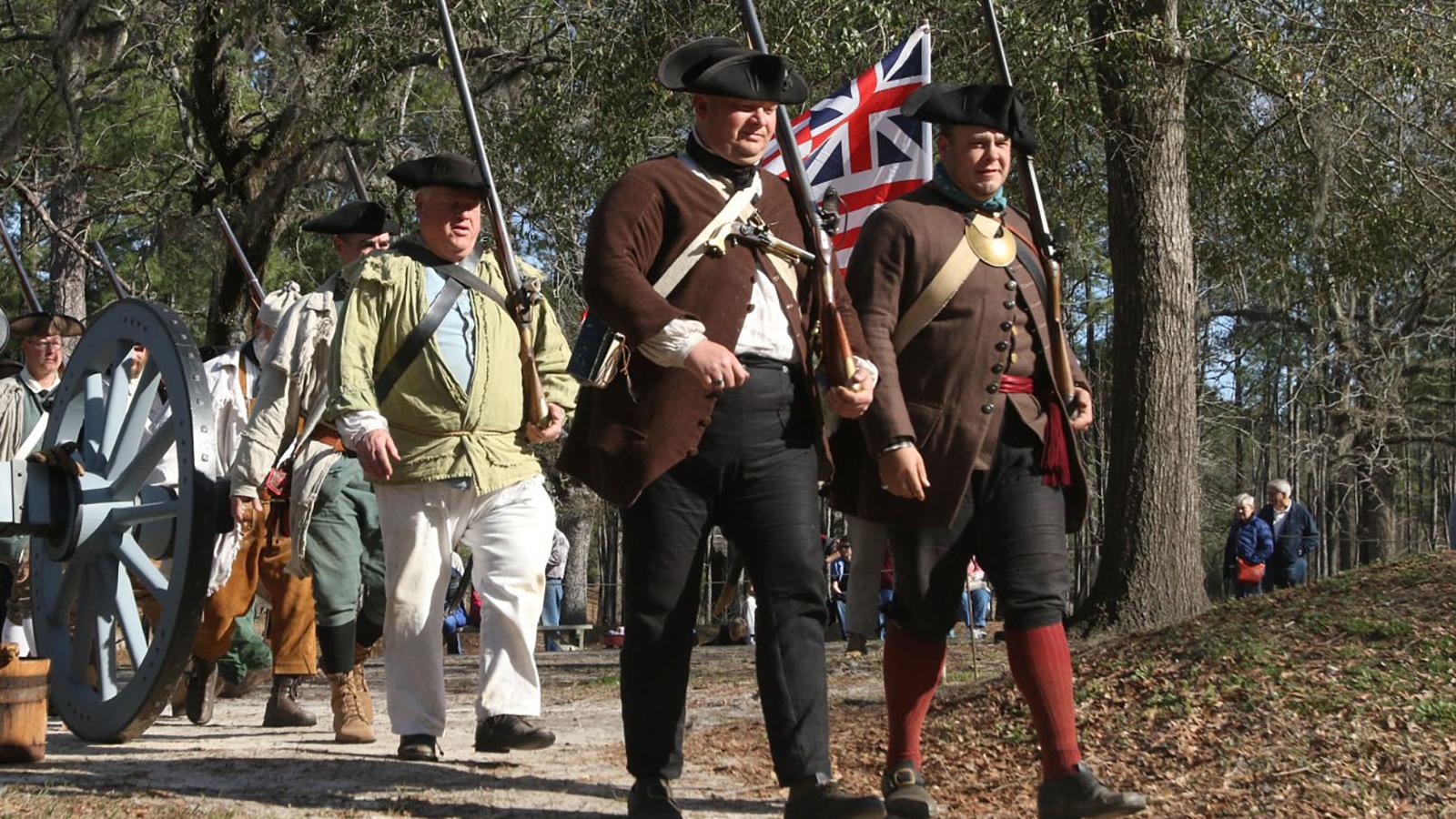 Men dressed in colonial clothing walking next to a cannon